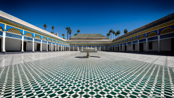 An ornate courtyard with intricate zellige tilework, stucco carvings, and lush greenery in Bahia Palace, Marrakech, showcasing the beauty of Moroccan palace architecture and design.