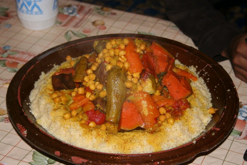 A plate filled with a large amount of couscous, a traditional Moroccan dish made of steamed semolina granules, topped with various vegetables and meat.