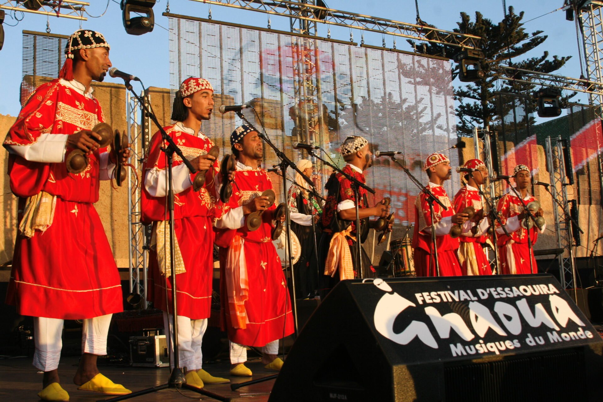 Alt text: A group of Gnawa musicians performing at the 15th Gnaoua World Music Festival in Essaouira. The musicians are playing traditional Moroccan instruments and wearing colorful clothing. The photo captures the vibrant and lively atmosphere of the festival, which celebrates music and dance from different cultures.