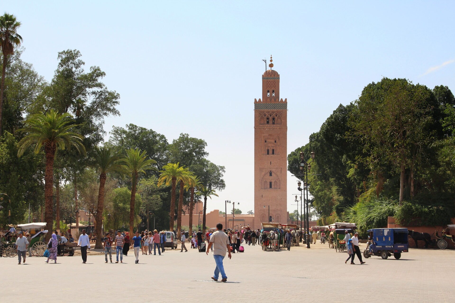 Image depicting Koutoubia Mosque square in Marrakech, Morocco, with several people walking around. The Koutoubia Mosque is visible in the background, showcasing the Islamic architectural style.