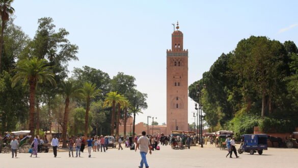 Image depicting Koutoubia Mosque square in Marrakech, Morocco, with several people walking around. The Koutoubia Mosque is visible in the background, showcasing the Islamic architectural style.