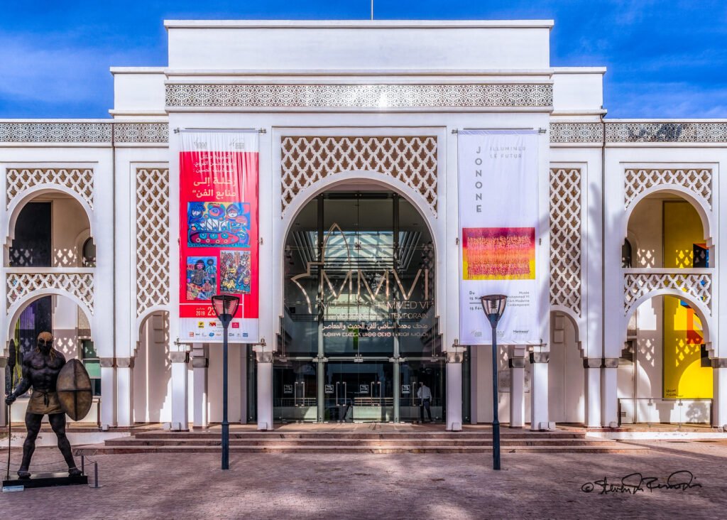 Exterior view of the Mohammed VI Museum of Modern Art in Rabat, Morocco, showcasing its sleek and minimalist design with a concrete facade and glass windows.