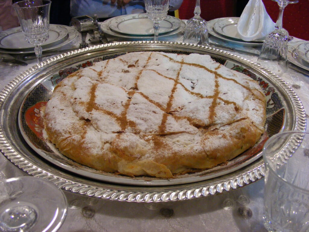 A beautifully presented dish of Pastilla, a traditional Moroccan delicacy, featuring layers of flaky pastry, tender meat, and aromatic spices, representing the rich history and cultural significance of Moroccan cuisine.