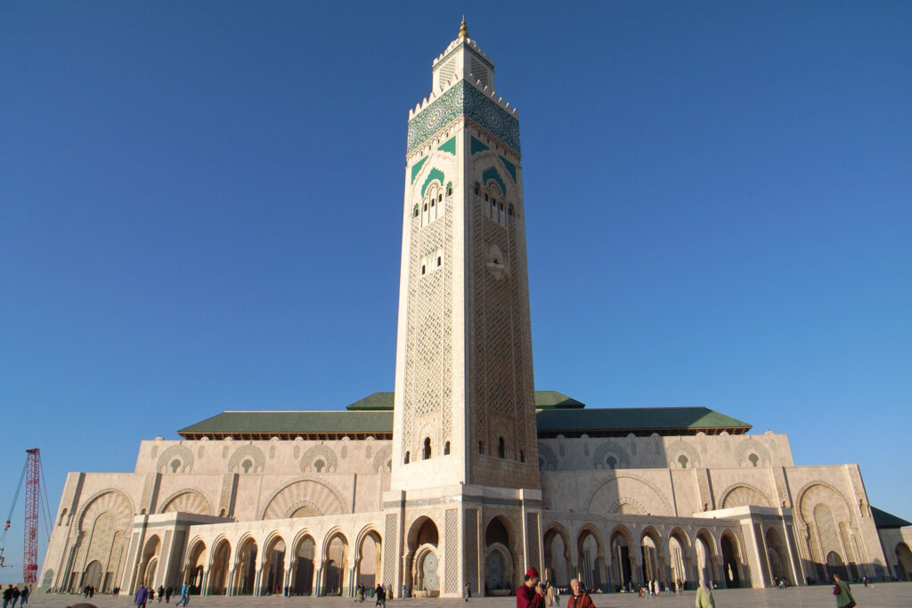 A photo of the exterior of the Hassan II Mosque in Casablanca, Morocco. The mosque is an impressive example of Islamic architecture, with a symmetrical facade, intricate details, and a towering minaret.