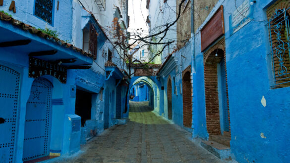 A view of one of the many blue-painted streets in Chefchaouen, Morocco. The buildings on both sides are painted in different shades of blue and there are lanterns hanging above the street.