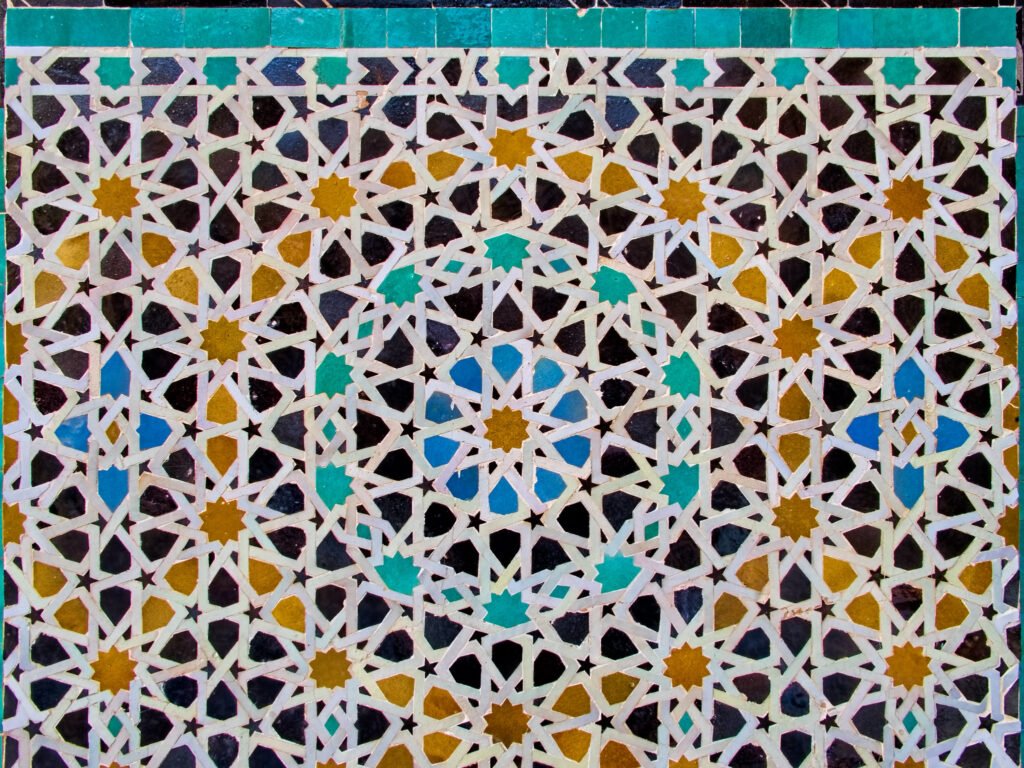 A close-up of intricate mosaic tilework covering the walls and ceiling inside the Bou Inania Madrasa, showcasing the art of Zellige, a traditional form of Moroccan mosaic design.