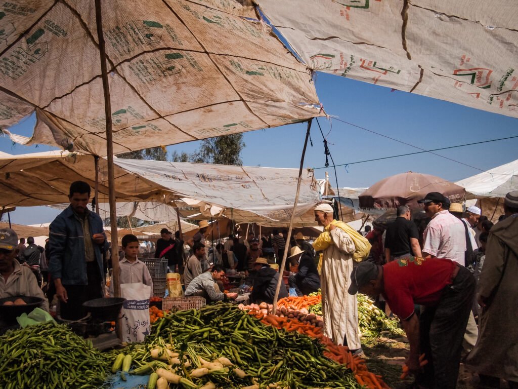 A photo of a colorful array of fresh vegetables piled up at a market in Morocco, showcasing the country's vibrant food culture and hospitality.