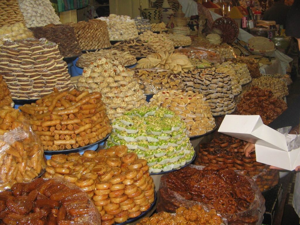 Assorted traditional Moroccan dishes and desserts such as baklava and date-filled pastries, displayed on a wooden table in Meknes.