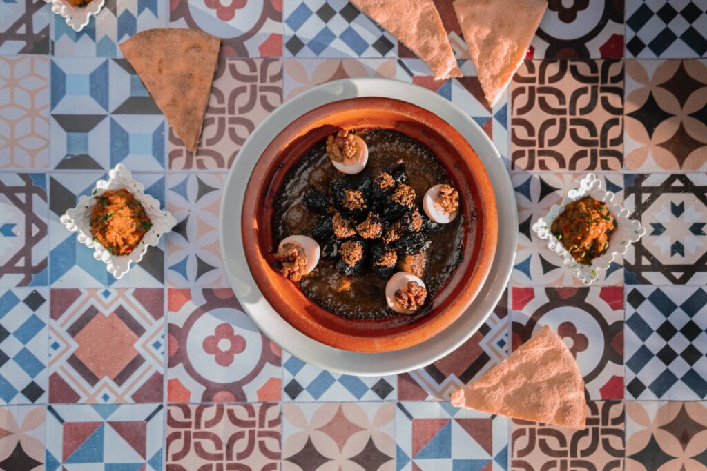 An example of pairing Tagines with Moroccan side dishes and desserts, featuring a platter of freshly baked bread served with a lamb tagine with dates and almonds, and a side of harissa sauce.