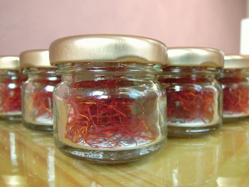 Image description: The image shows several small pots filled with saffron threads in vibrant shades of red and orange. The pots are displayed on a table with a decorative tablecloth in the background. The photo appears to be taken at the Taliouine Saffron Festival.