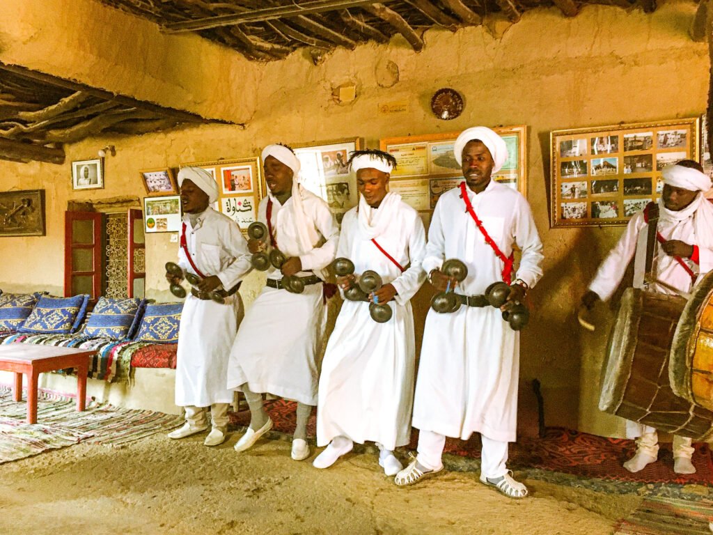 A group of Gnawa musicians wearing traditional clothing and playing musical instruments in the Sahara Desert, Morocco.