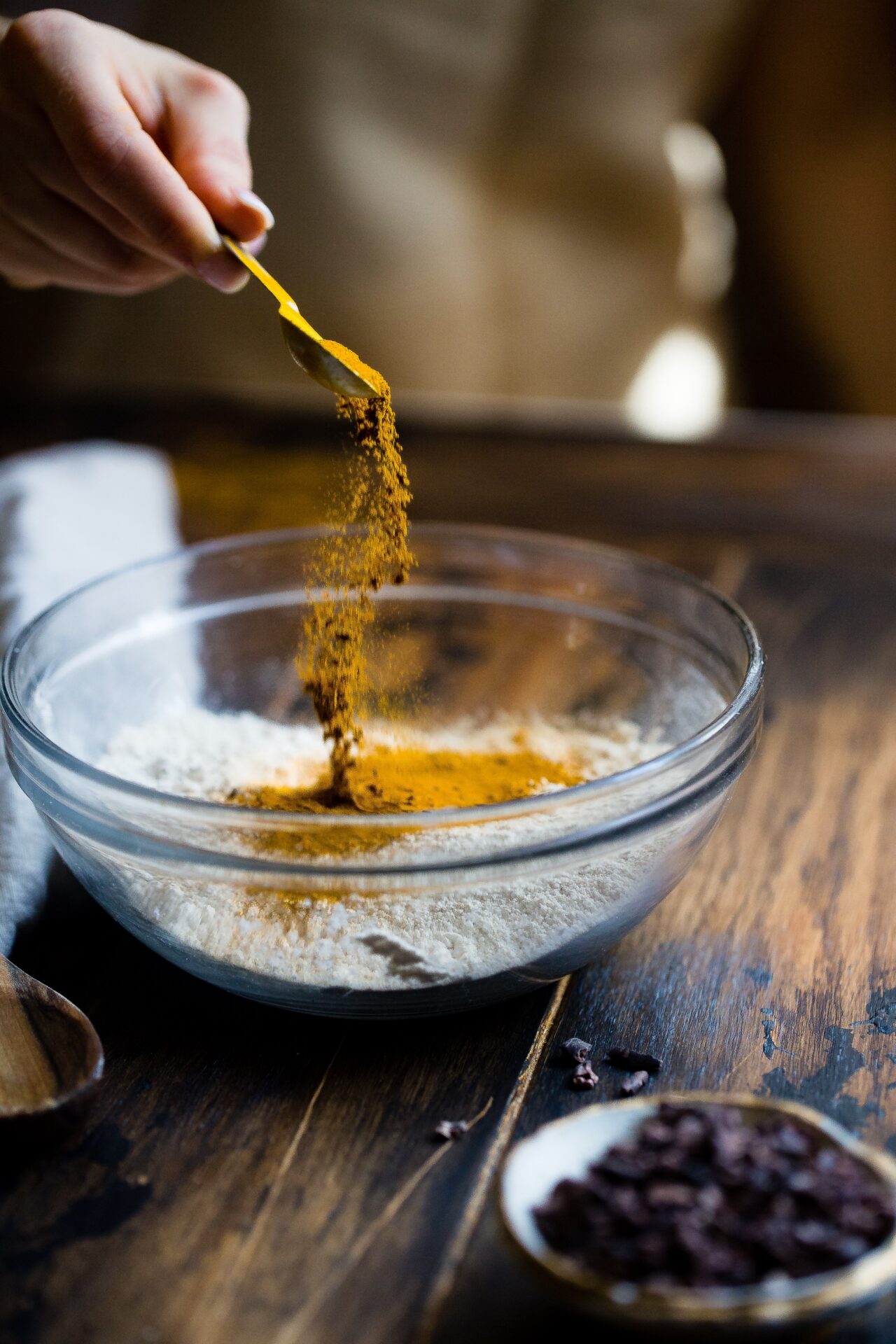 A person pouring Moroccan spices onto a clear glass bowl as an example of using these spices in international cuisine.