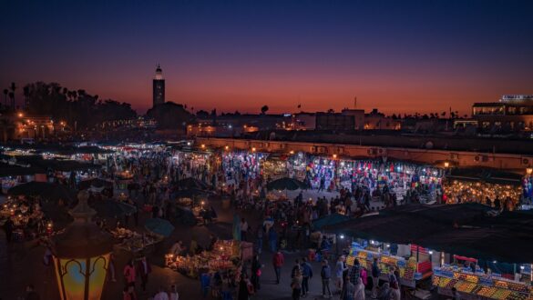 People gathered in Jemaa el-Fnaa Square at night, with food vendors, musicians, and street performers in the background.