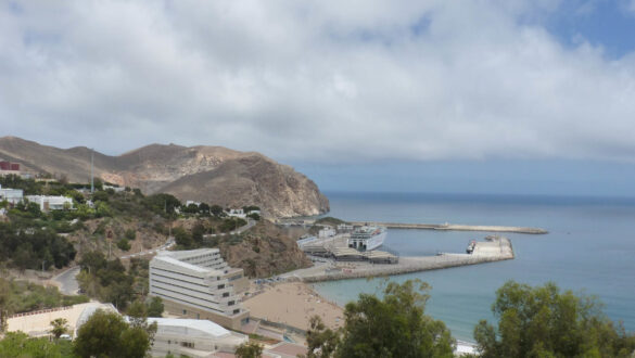 A panoramic view of Al Hoceïma, a hidden gem, featuring pristine sandy beaches, turquoise waters, and a charming coastal town. The image showcases a picturesque scene with a row of colorful buildings lining the shoreline, complemented by palm trees and a clear blue sky, inviting visitors to relax and indulge in the beauty of this coastal paradise.