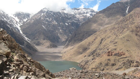 Panoramic view of Lake Ifni surrounded by the towering Atlas Mountains, their peaks covered in a blanket of glistening white snow.