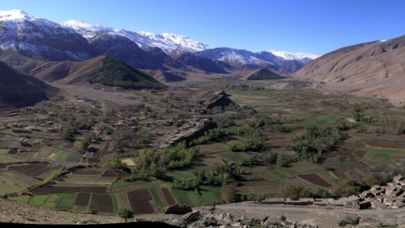 A breathtaking panoramic view of the snow-covered Aït Bouguemez Valley in the High Atlas Mountains. The image captures the picturesque landscape with terraced hills and white snow-capped mountains, showcasing the natural beauty of this hidden gem in Morocco